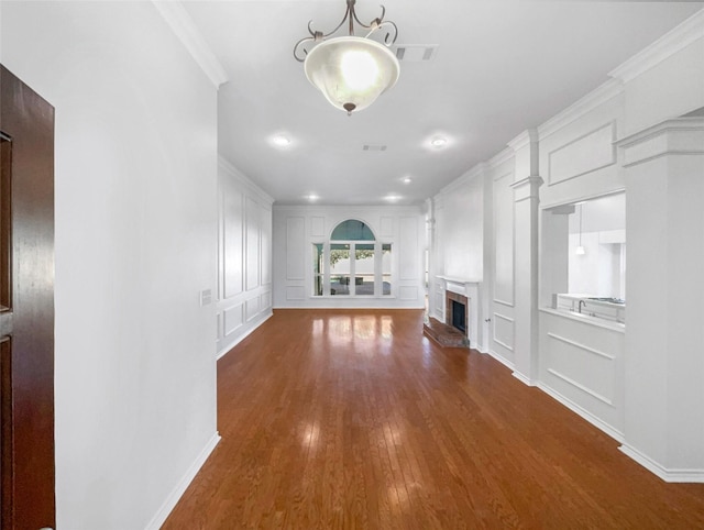 unfurnished living room with a decorative wall, dark wood-type flooring, a fireplace, visible vents, and ornamental molding