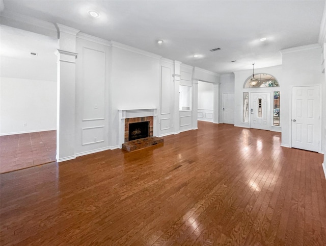 unfurnished living room with a fireplace with raised hearth, crown molding, visible vents, dark wood-style floors, and ornate columns