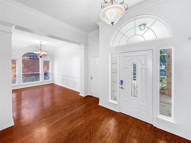 entryway with dark wood finished floors, wainscoting, ornamental molding, ornate columns, and a chandelier