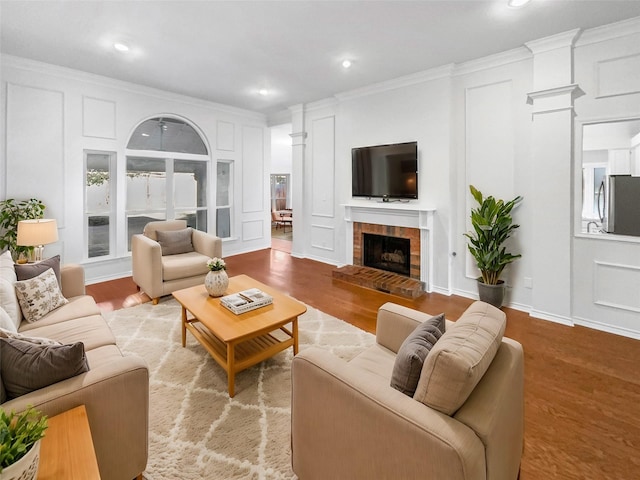 living area featuring crown molding, a fireplace with raised hearth, a decorative wall, and wood finished floors