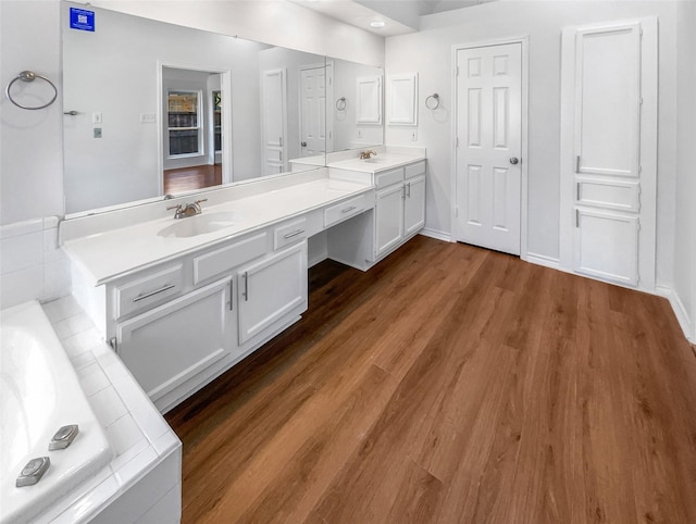 bathroom featuring double vanity, tiled tub, a sink, and wood finished floors