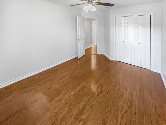 unfurnished bedroom featuring dark wood-type flooring, a closet, baseboards, and a ceiling fan