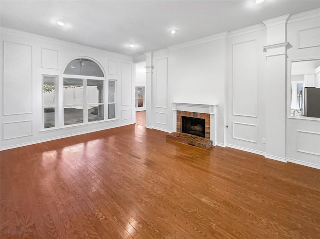 unfurnished living room featuring ornamental molding, a fireplace with raised hearth, a decorative wall, and wood finished floors