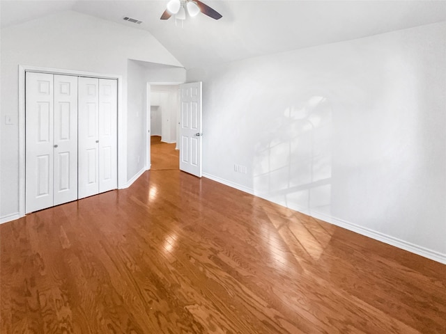 unfurnished bedroom featuring lofted ceiling, a closet, visible vents, and wood finished floors