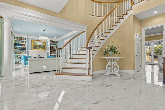 foyer entrance with french doors, a towering ceiling, a chandelier, ornamental molding, and ornate columns