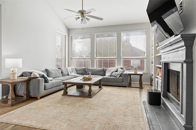 living area featuring a healthy amount of sunlight, light wood-style floors, a fireplace with raised hearth, and lofted ceiling