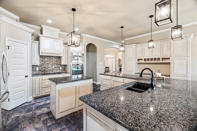 kitchen with a center island with sink, sink, dark stone counters, stainless steel appliances, and hanging light fixtures