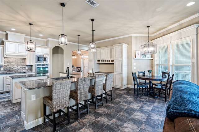 kitchen featuring appliances with stainless steel finishes, hanging light fixtures, a kitchen breakfast bar, dark stone counters, and a large island with sink