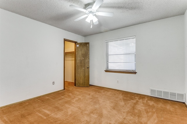 unfurnished bedroom with a closet, a walk in closet, a textured ceiling, ceiling fan, and light colored carpet