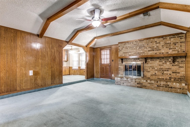 unfurnished living room featuring a brick fireplace, light colored carpet, wood walls, vaulted ceiling with beams, and a textured ceiling