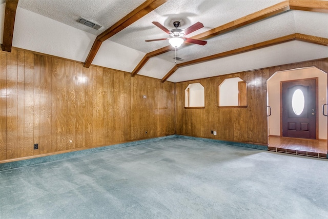 carpeted empty room featuring ceiling fan, wood walls, lofted ceiling with beams, and a textured ceiling