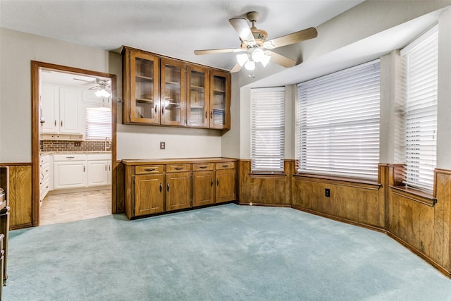 kitchen with light carpet, ceiling fan, and wood walls