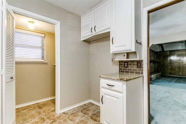 kitchen featuring light tile patterned floors, light stone counters, white cabinets, and backsplash