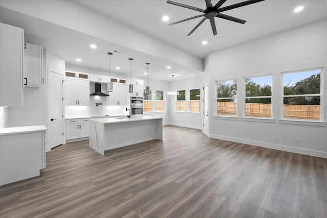 kitchen with white cabinetry, a center island with sink, sink, wall chimney exhaust hood, and pendant lighting