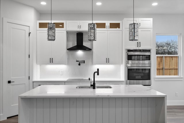 kitchen featuring double oven, sink, wall chimney exhaust hood, and light stone counters