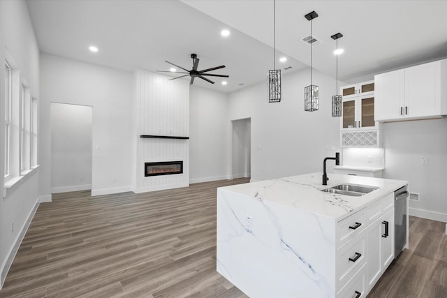 kitchen featuring an island with sink, white cabinetry, sink, and light stone counters