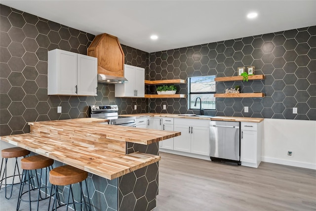 kitchen featuring appliances with stainless steel finishes, wooden counters, a breakfast bar area, sink, and white cabinetry