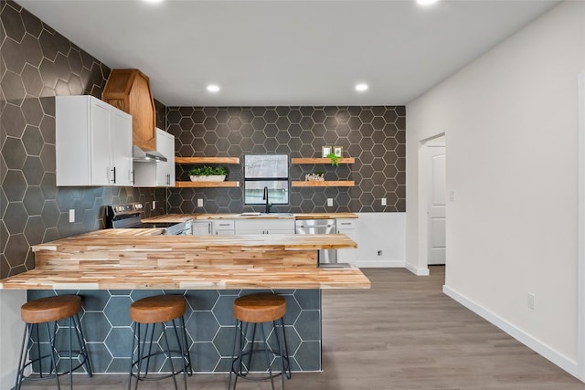 kitchen featuring appliances with stainless steel finishes, white cabinetry, a kitchen breakfast bar, and butcher block countertops