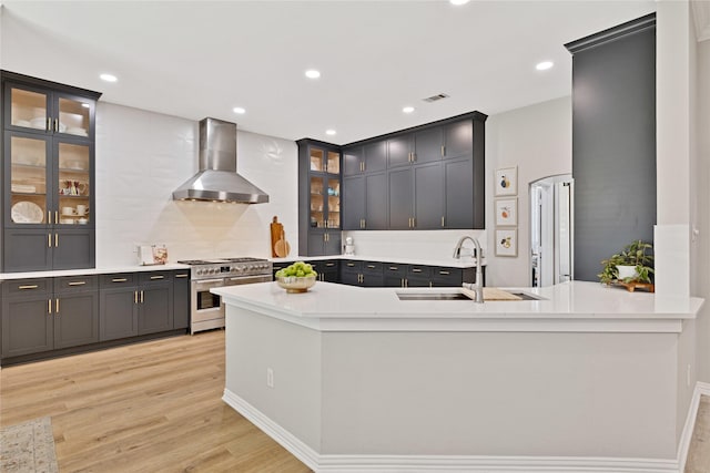 kitchen with wall chimney range hood, glass insert cabinets, range with two ovens, and light countertops