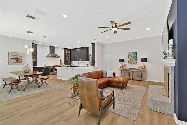 living area with visible vents, light wood-style flooring, ornamental molding, a brick fireplace, and recessed lighting