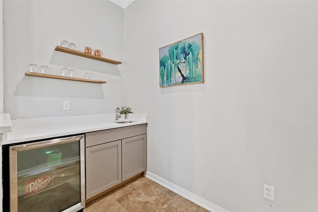 bar with beverage cooler, a sink, and baseboards