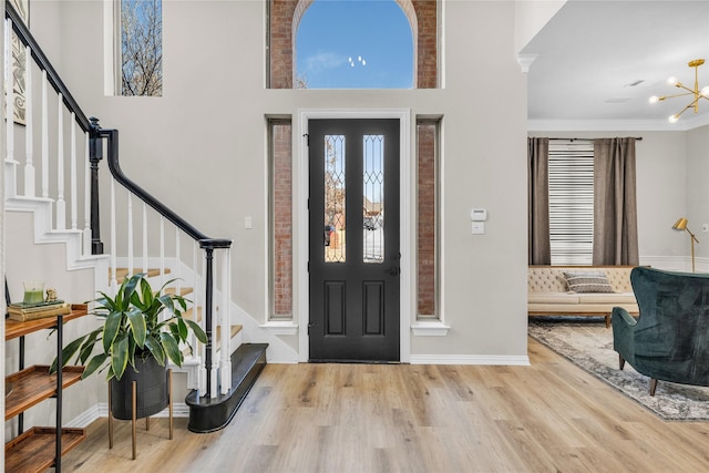 entryway with light wood finished floors, a high ceiling, stairs, crown molding, and a chandelier