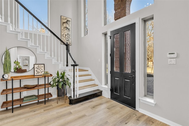 entryway featuring a high ceiling, stairway, light wood-style flooring, and baseboards