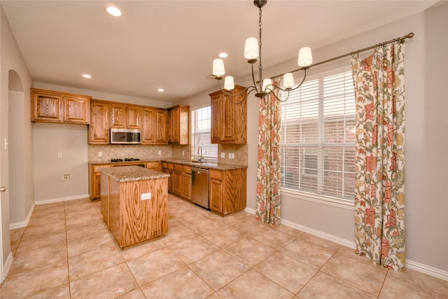 kitchen with tasteful backsplash, stainless steel appliances, light stone countertops, a kitchen island, and sink