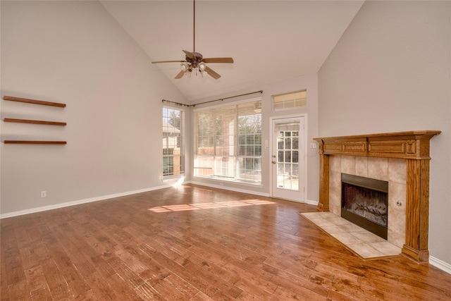 unfurnished living room featuring ceiling fan, light hardwood / wood-style flooring, high vaulted ceiling, and a tiled fireplace