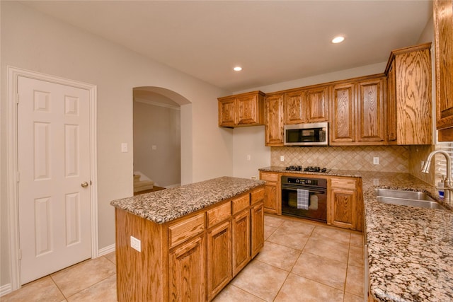 kitchen featuring sink, light stone counters, a center island, oven, and tasteful backsplash