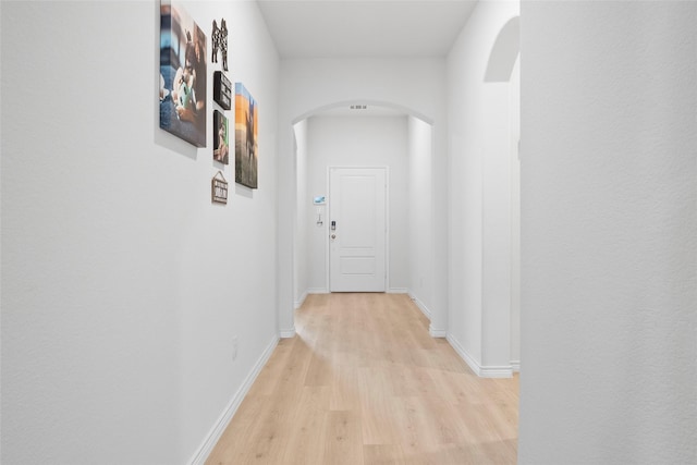 corridor featuring arched walkways, light wood-style flooring, and baseboards