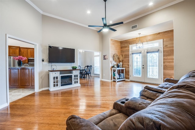 living room featuring wood walls, light hardwood / wood-style floors, french doors, and a towering ceiling