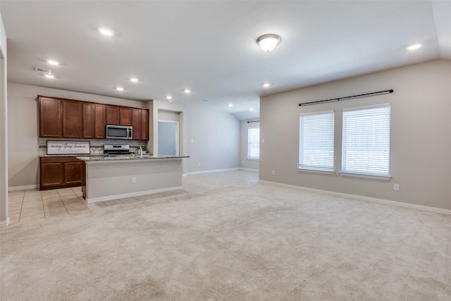 kitchen featuring light carpet, a center island with sink, decorative backsplash, open floor plan, and stainless steel appliances