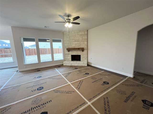 unfurnished living room with ceiling fan and a stone fireplace