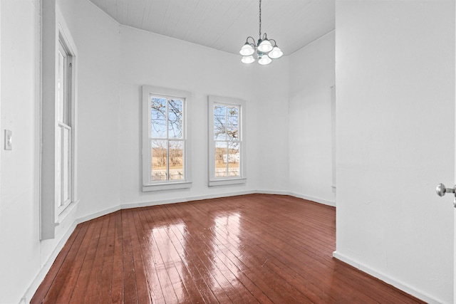 unfurnished dining area with vaulted ceiling, an inviting chandelier, and hardwood / wood-style floors