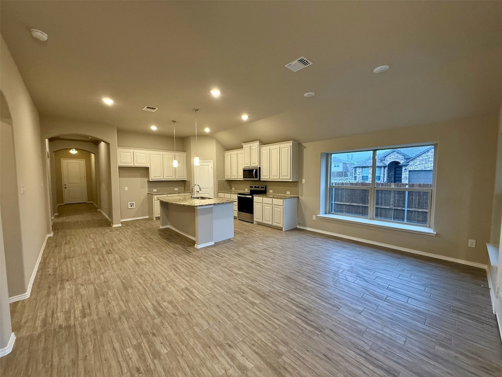 kitchen featuring appliances with stainless steel finishes, an island with sink, light stone countertops, decorative light fixtures, and white cabinetry