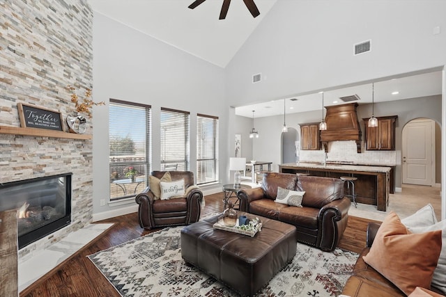 living area featuring arched walkways, lofted ceiling, ceiling fan, light wood-type flooring, and a fireplace