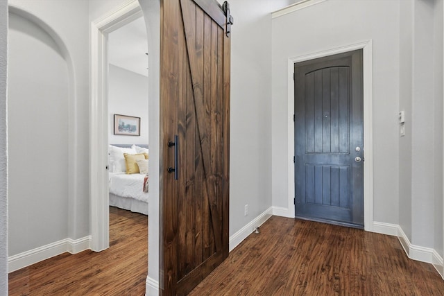 entrance foyer featuring arched walkways, a barn door, dark wood finished floors, and baseboards