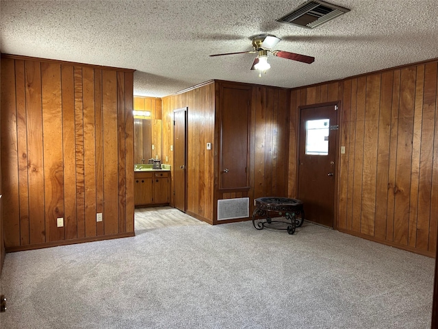 interior space with a textured ceiling, wooden walls, light colored carpet, and ceiling fan