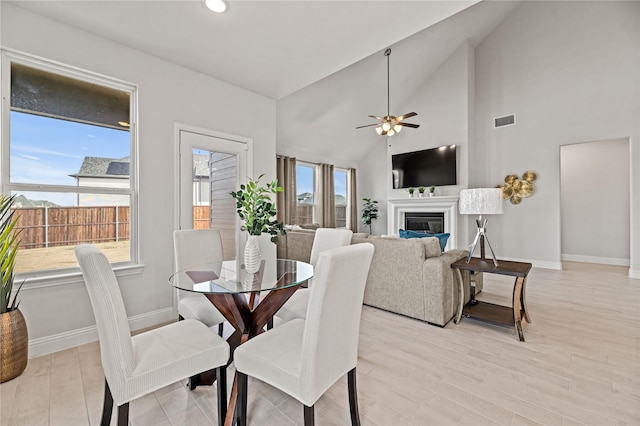 dining space with ceiling fan, baseboards, vaulted ceiling, and light wood-style flooring