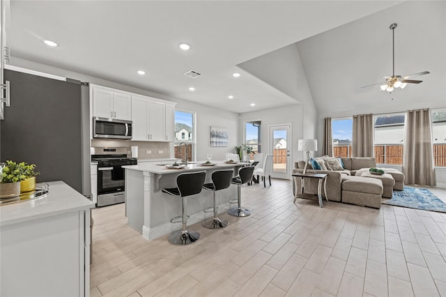 kitchen featuring visible vents, open floor plan, a kitchen bar, light countertops, and appliances with stainless steel finishes