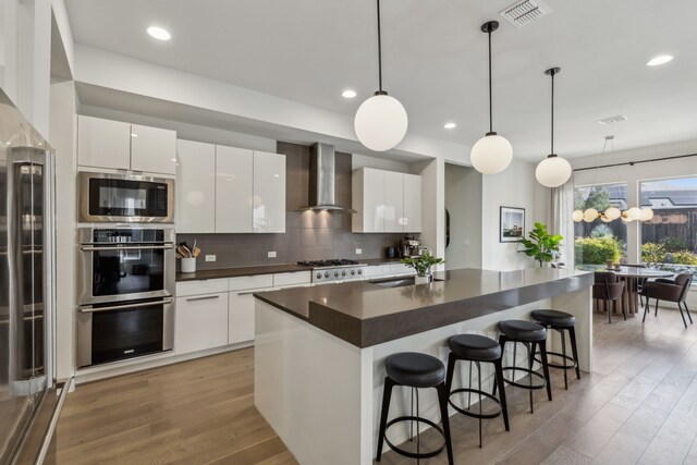 4112 Heatherton Dr, Celina, TX 75009 - kitchen with wall chimney exhaust hood, appliances with stainless steel finishes, dark countertops, modern cabinets, and light wood-style flooring
