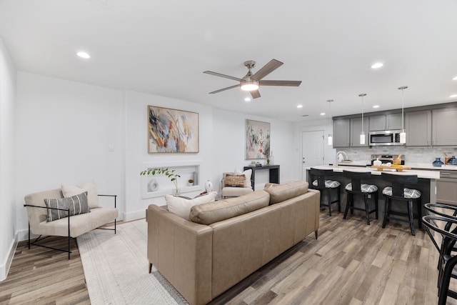 living room featuring ceiling fan, light hardwood / wood-style flooring, and sink