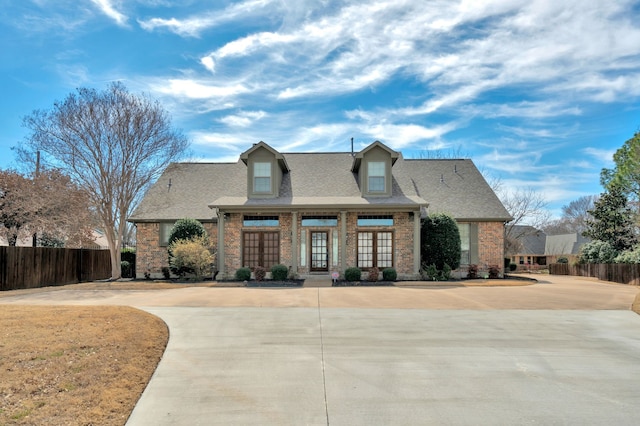 view of front facade featuring concrete driveway, french doors, fence, and brick siding