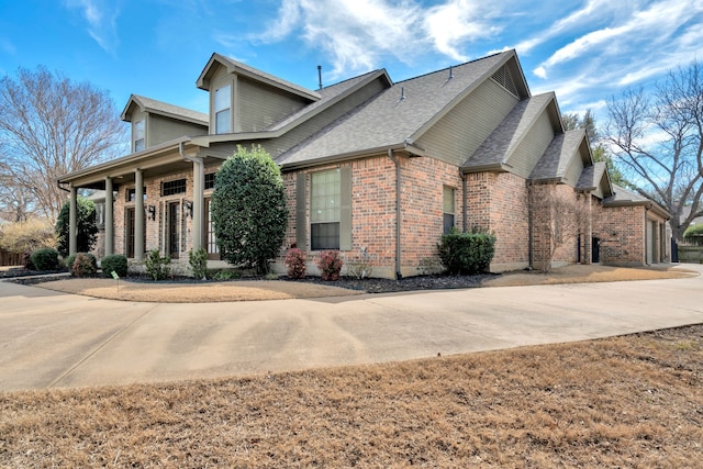 view of front facade featuring driveway, roof with shingles, an attached garage, and brick siding