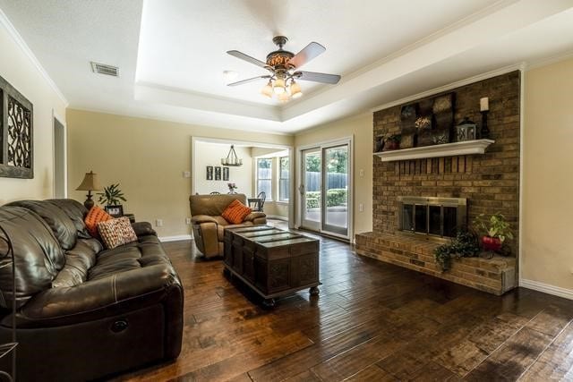 living room featuring a raised ceiling, crown molding, dark hardwood / wood-style floors, and a fireplace