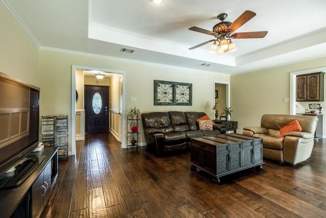 living room featuring ceiling fan, a tray ceiling, dark hardwood / wood-style floors, and ornamental molding