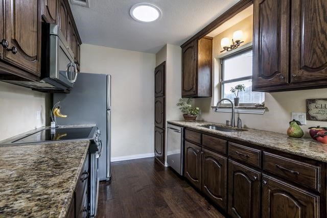 kitchen with appliances with stainless steel finishes, dark brown cabinets, light stone counters, dark hardwood / wood-style flooring, and sink