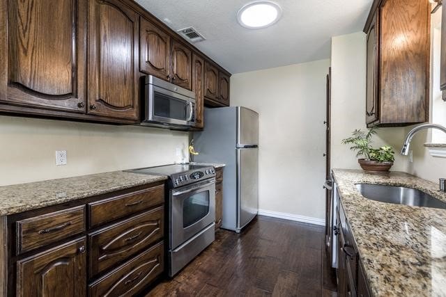 kitchen featuring appliances with stainless steel finishes, light stone countertops, and dark brown cabinets