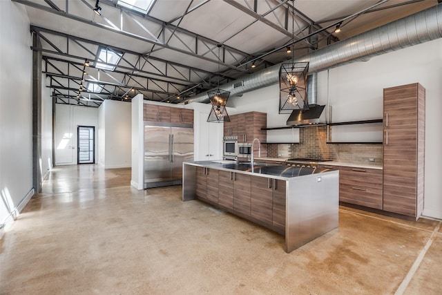 kitchen with a high ceiling, stainless steel appliances, decorative backsplash, sink, and a kitchen island with sink